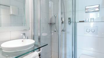 A modern bathroom with a glass-enclosed shower, a glass sink, and a white toilet.