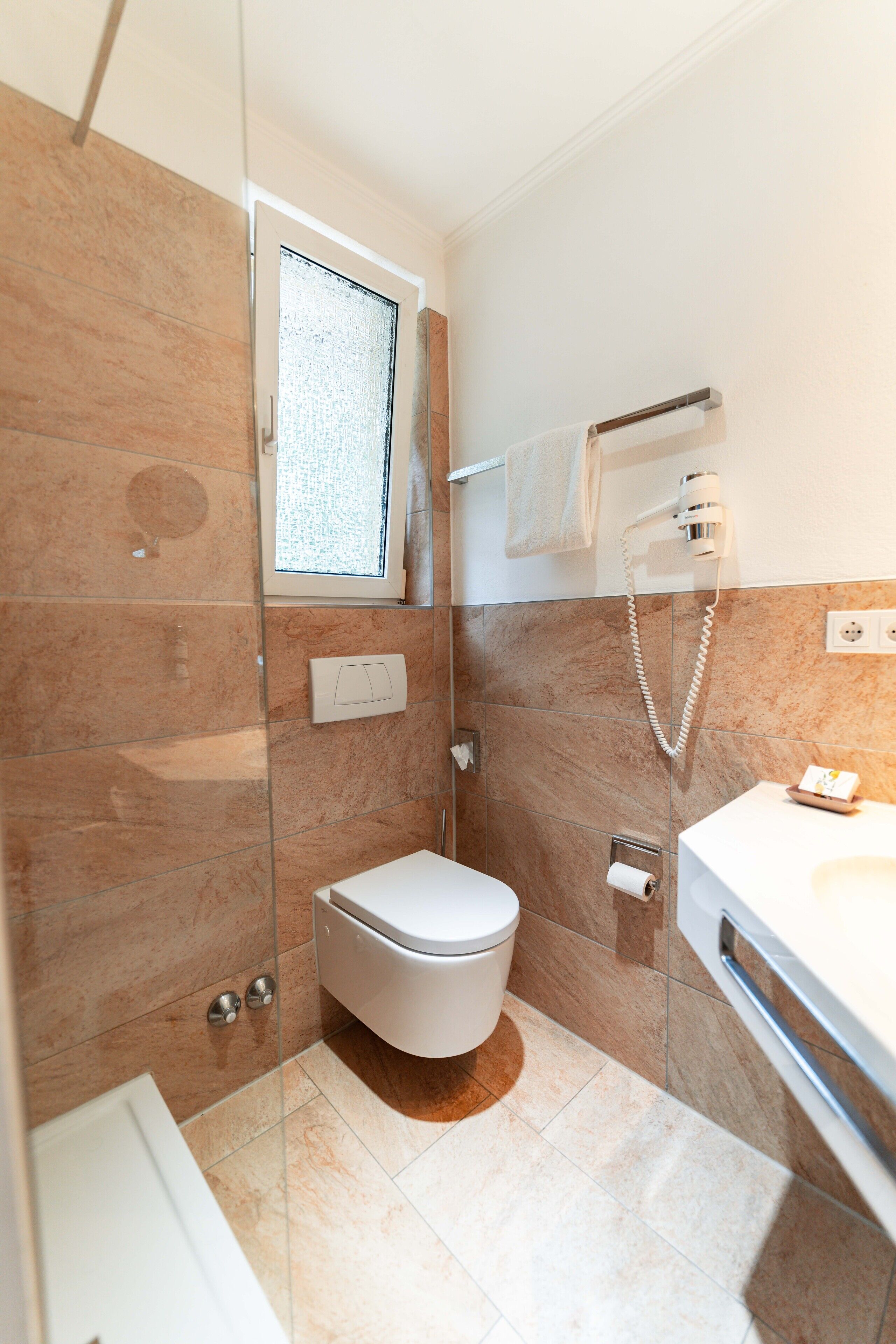 A modern bathroom with a glass shower enclosure, a toilet, a sink, and a towel rack.