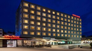 Un hotel de varios pisos con un llamativo letrero de "VIENNA HOUSE", un restaurante llamado "BULL&BONITO" en la planta baja y un área de estar al aire libre cubierta.