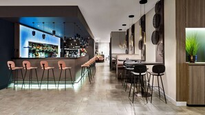 Un bar moderno con una barra larga, varios taburetes y una zona de estar con mesas y sillas.