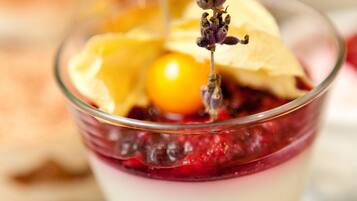 A dessert in a clear glass with layers of cream and berries, garnished with a yellow fruit and a sprig of lavender.
