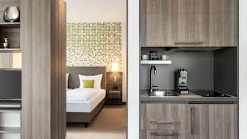 Una habitación de hotel moderna con cama, mesita de noche y una pared con un diseño de puntos. La habitación tiene un armario de madera y una kitchenette con un lavabo y una máquina de café.