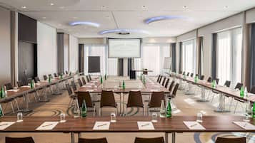 Une salle de conférence avec de longues tables, des chaises et un grand écran à l’avant.