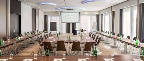A conference room with long tables, chairs, and a large screen at the front.