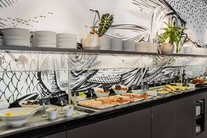 Un buffet proposant une variété de plats et d’assiettes, agrémenté de plantes décoratives et placé devant un mur orné de motifs.