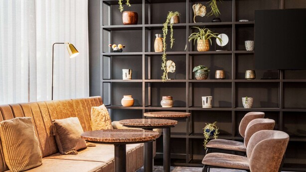 Un interior moderno con un sofá, mesas redondas, sillas, una estantería con objetos decorativos y un televisor de pantalla plana.