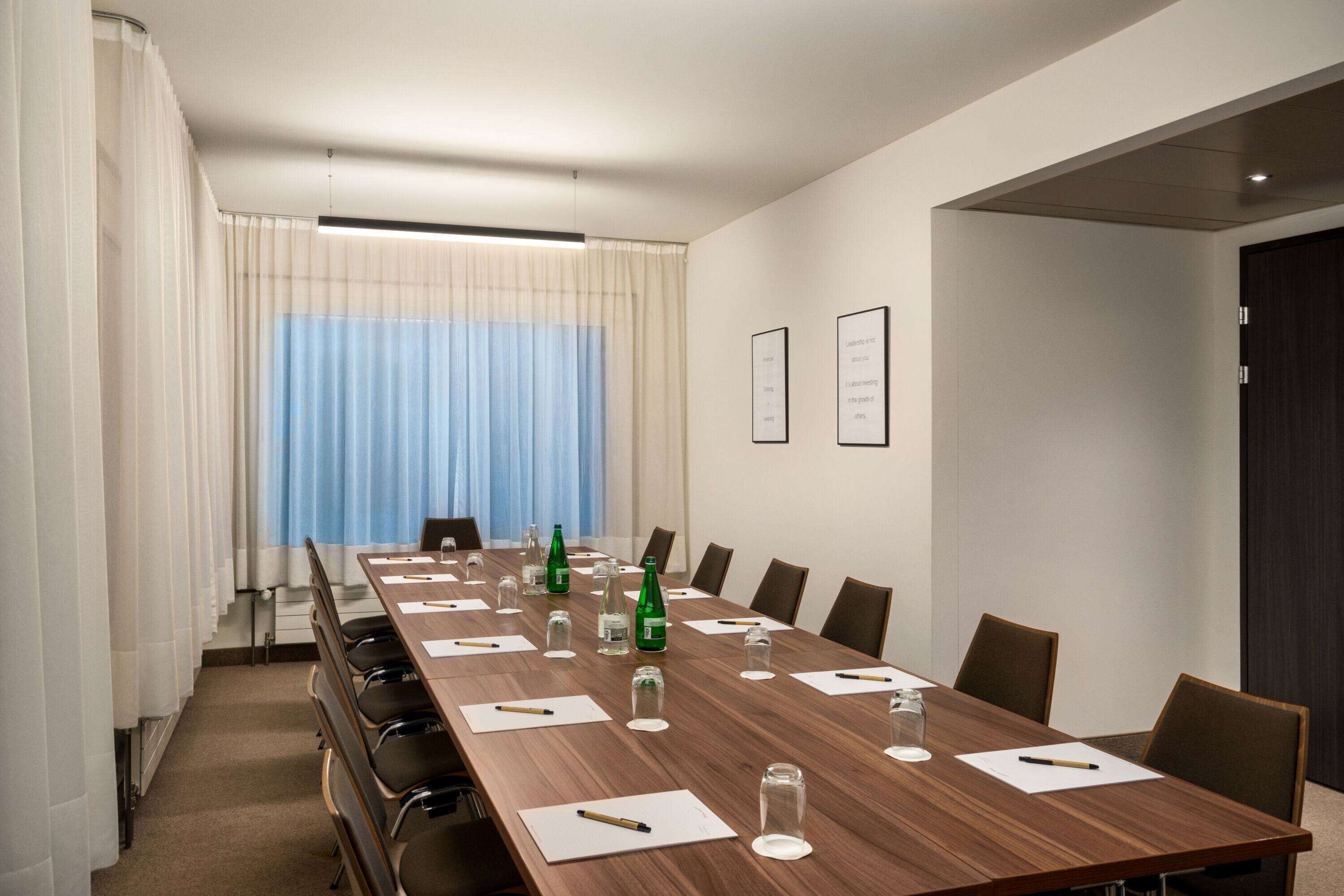 A conference room with a long wooden table, chairs, and a window with curtains.
