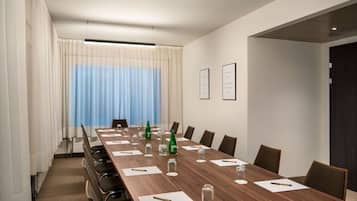 A conference room with a long wooden table, chairs, and a window with curtains.