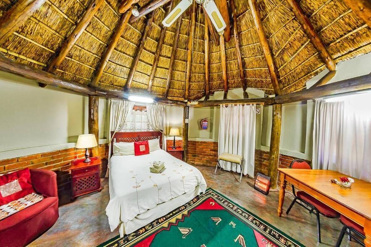 Ein Zimmer mit Strohdach, einem Bett mit weißer Bettdecke, einem roten Sofa, einem Holztisch und einem grün gemusterten Teppich.