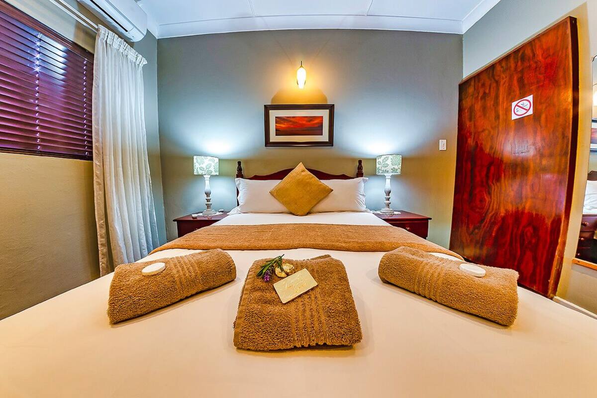 Ein Hotelzimmer mit einem großen Bett, zwei Nachttischen mit Lampen, einer Holztür mit Rauchverbotsschild und einem gerahmten Bild über dem Bett.