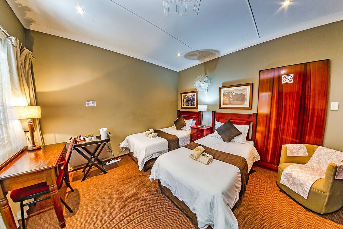 Ein Hotelzimmer mit zwei Betten, einem Schreibtisch, einem Stuhl, einer Lampe und einem Ventilator.