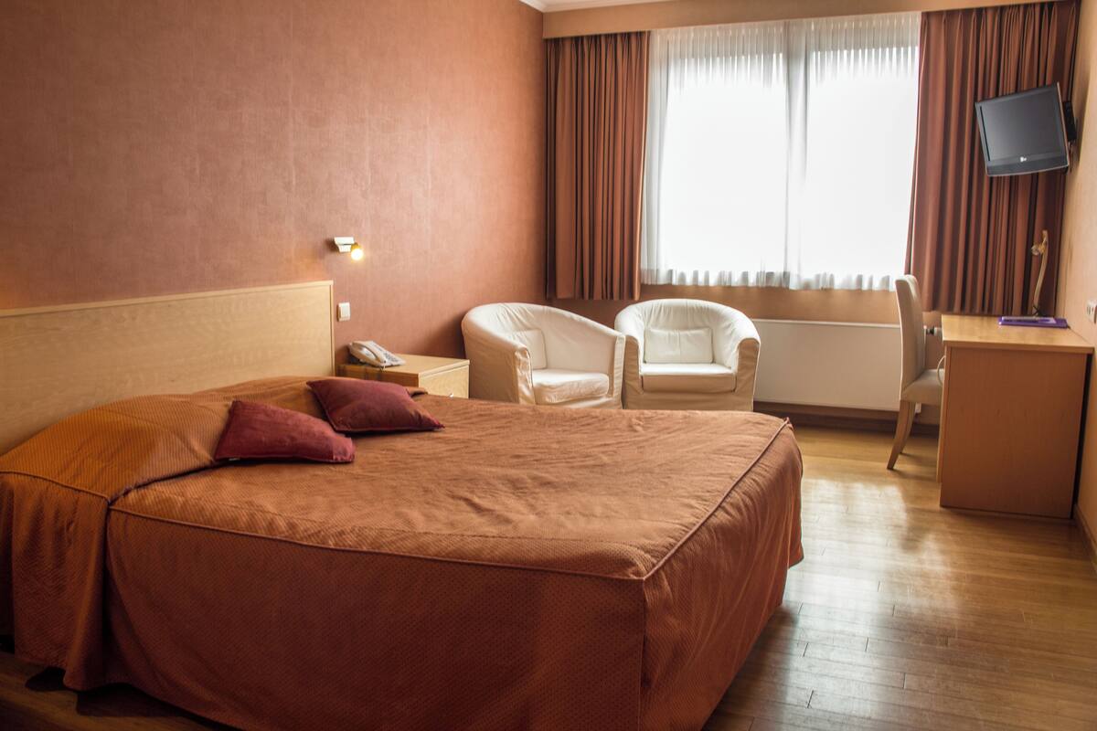 Ein Hotelzimmer mit einem großen Bett, einem Schreibtisch, einem Sessel und einem Fernseher.