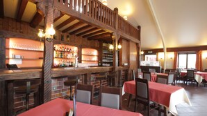 Een restaurant met houten inrichting, een bar en tafels met rode tafelkleden.