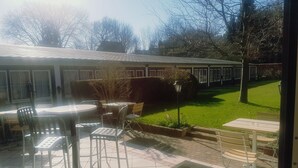 Een terras met zitplaatsen buiten, een gazon en een gebouw op de achtergrond.