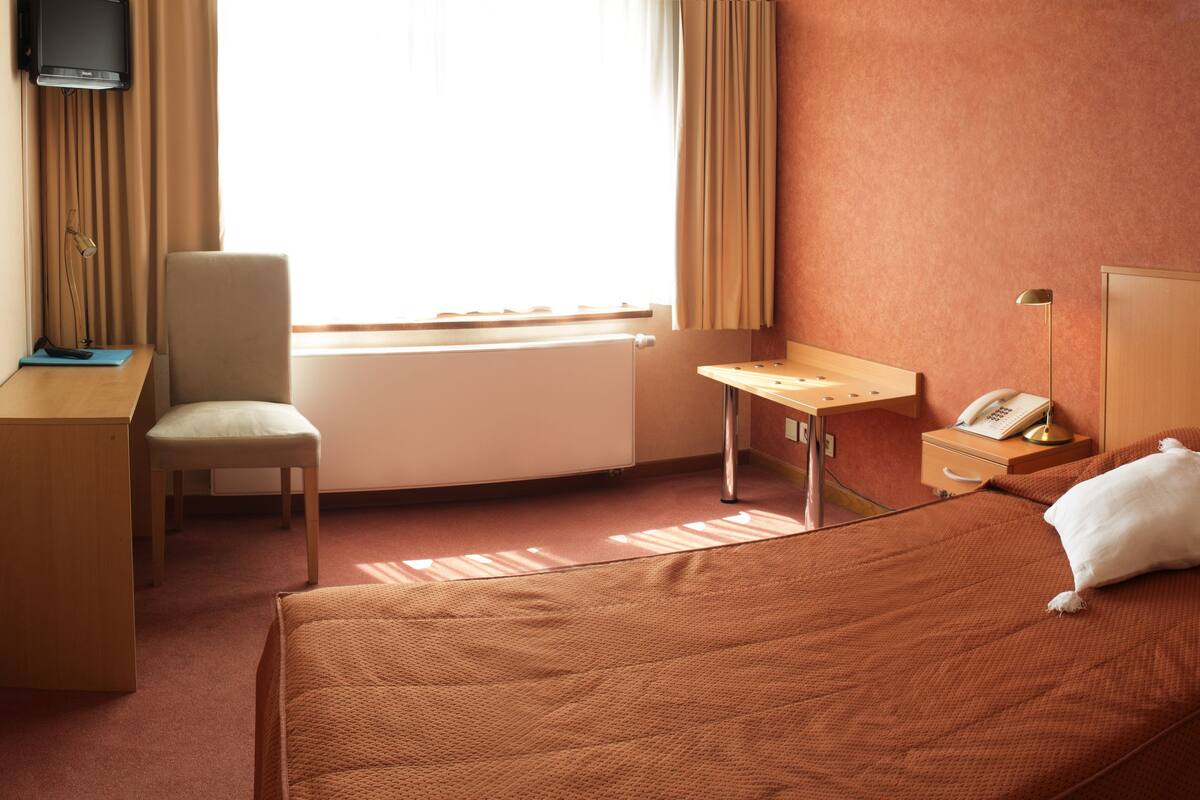 Ein Hotelzimmer mit Bett, Schreibtisch, Stuhl, Fernseher und Telefon.