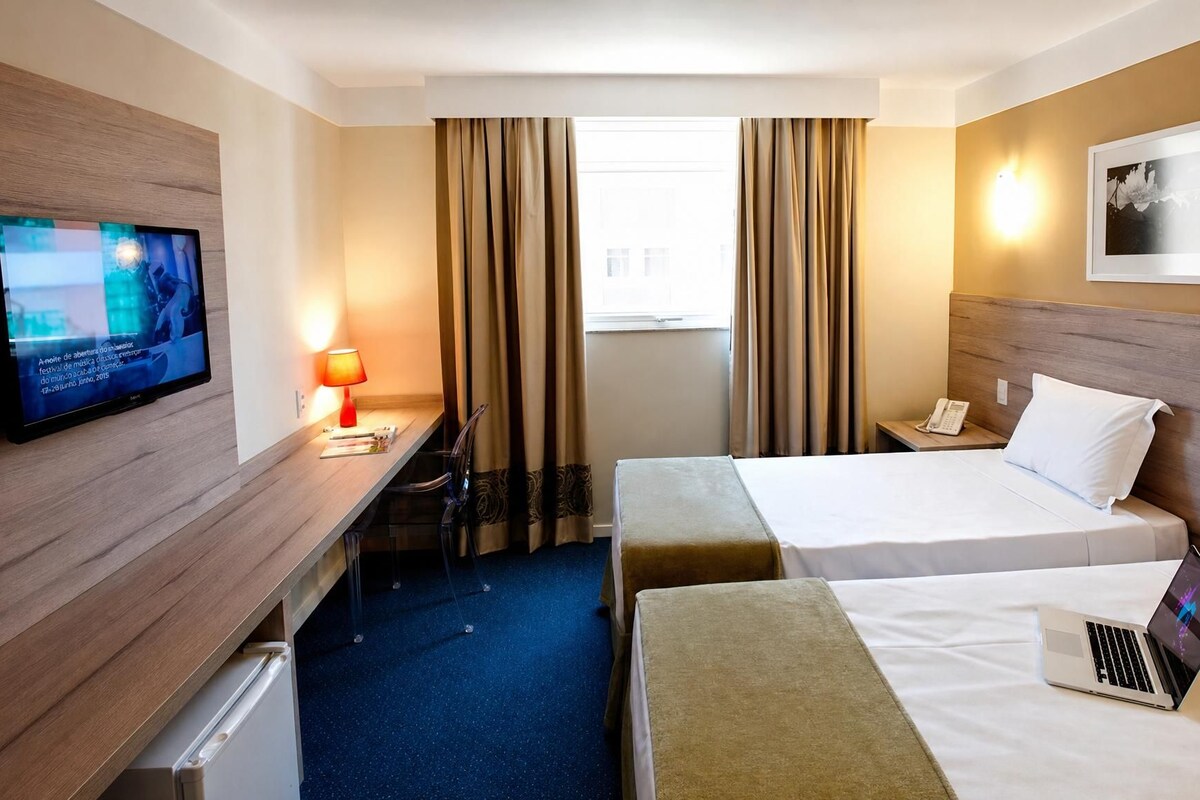 A hotel room with a bed, a desk with a computer, a TV, and a phone.