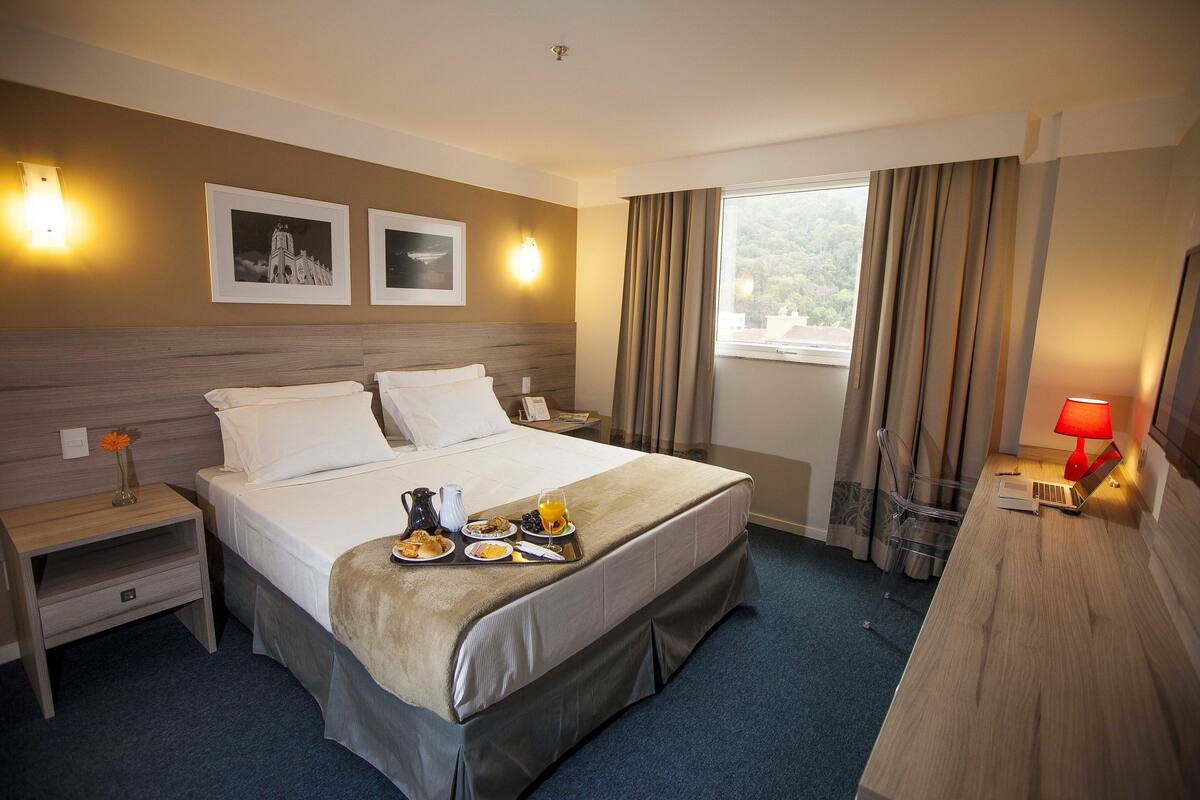 Una habitación de hotel con cama, mesita de noche, escritorio y ventana con cortinas.