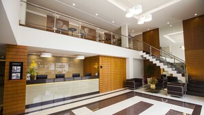 A modern hotel lobby with a reception desk, seating area, staircase, and a glass railing on the upper level. - Intercity Teresopolis (Teresópolis)