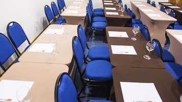 A conference room with rows of blue chairs, beige tables, and water glasses.