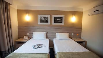 A hotel room with two beds, a wooden headboard, wall-mounted lamps, and a framed picture above each bed.