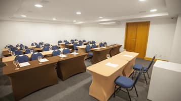 Ein Konferenzraum mit mehreren Tischen und Stühlen, ausgestattet mit Mikrofonen und Gläsern mit Wasser.