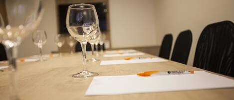 A conference room with a long table, several wine glasses, and papers with pens.
