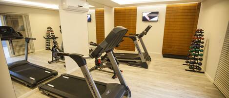 Uma academia com esteiras, bicicleta ergométrica e suporte de halteres na parede.
