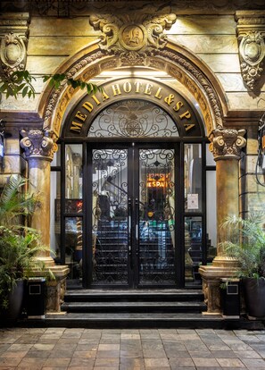 A hotel entrance with ornate gold detailing, a large arched sign, and a glass door with a reflection of the interior. - Hanoi Media Hotel and Spa (Hanoi)