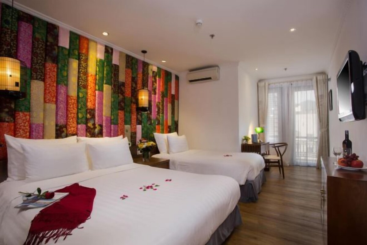 A hotel room with two beds, a TV, a desk with a chair, and a window with curtains.