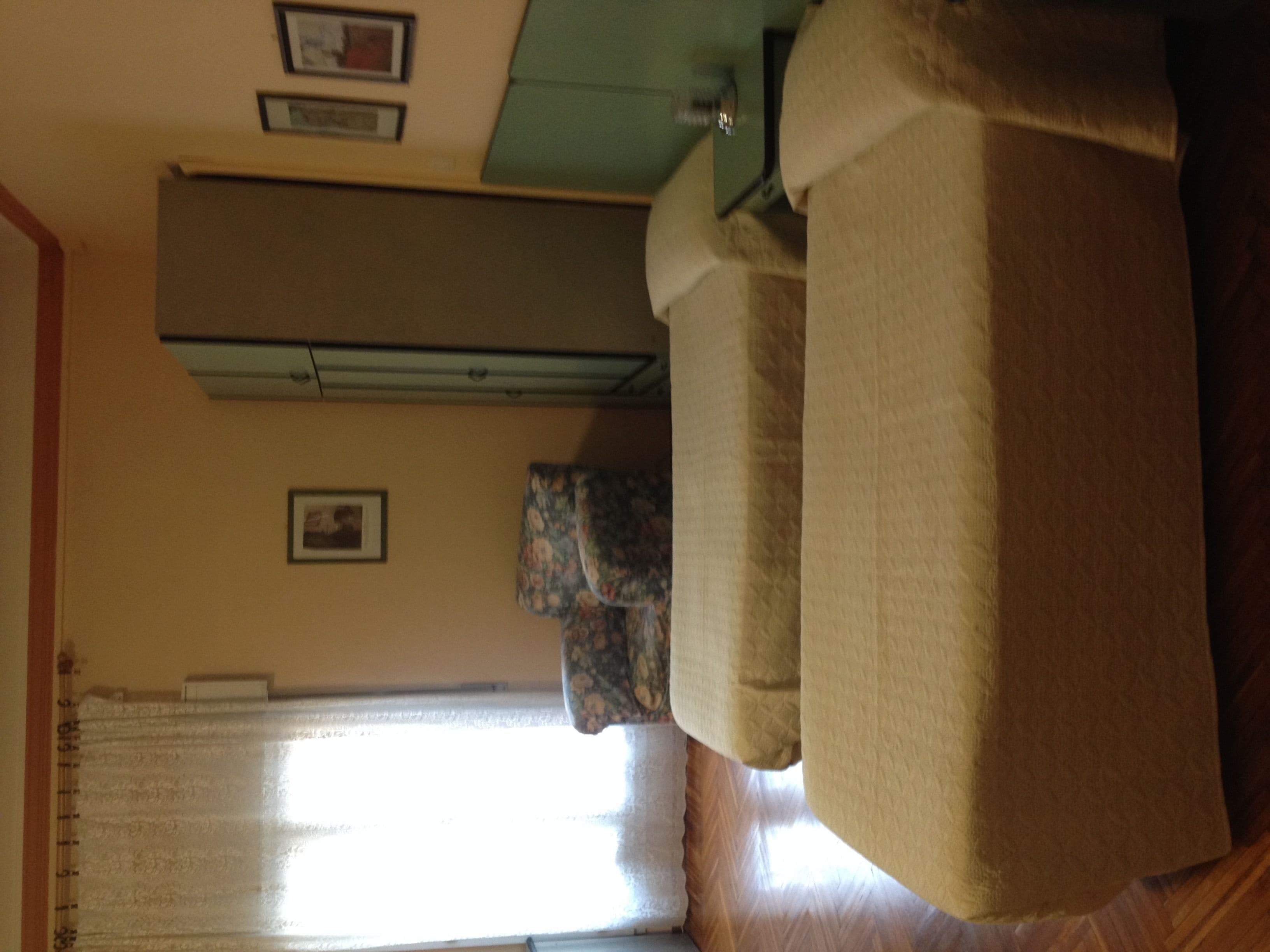 A living room with a sofa, a window with curtains, and a wall-mounted air conditioning unit.