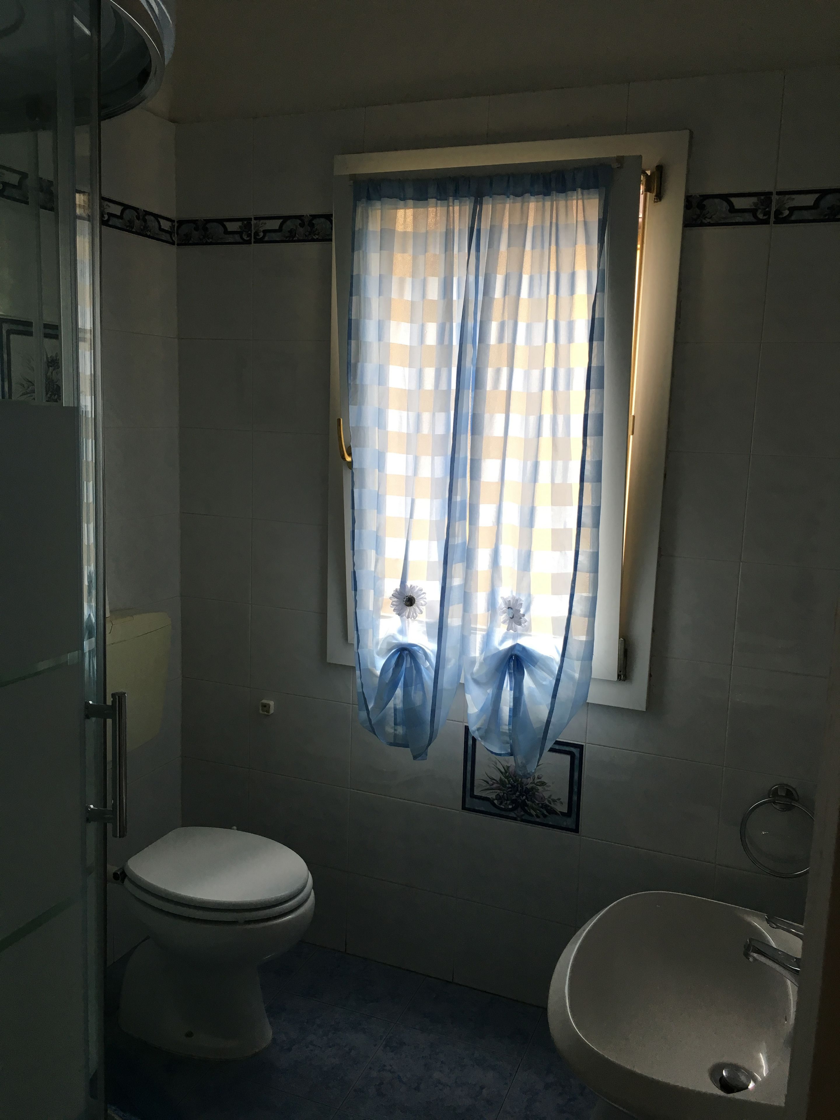 Une salle de bain avec des toilettes, un lavabo et une fenêtre ornée d’un rideau à carreaux.