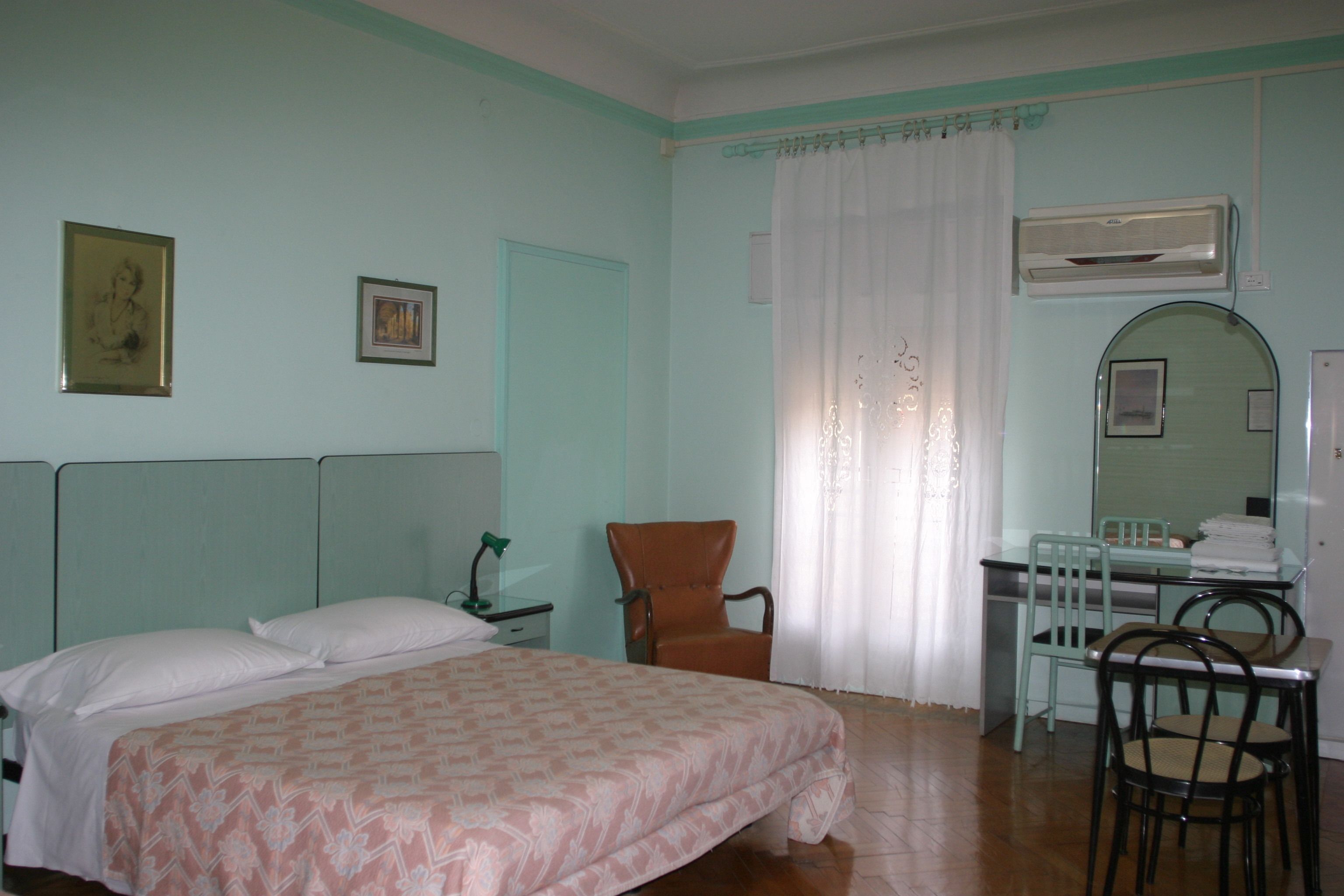 A bedroom with a bed, a chair, a desk, and a mirror.