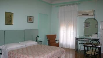 A bedroom with a bed, a chair, a desk, and a mirror.