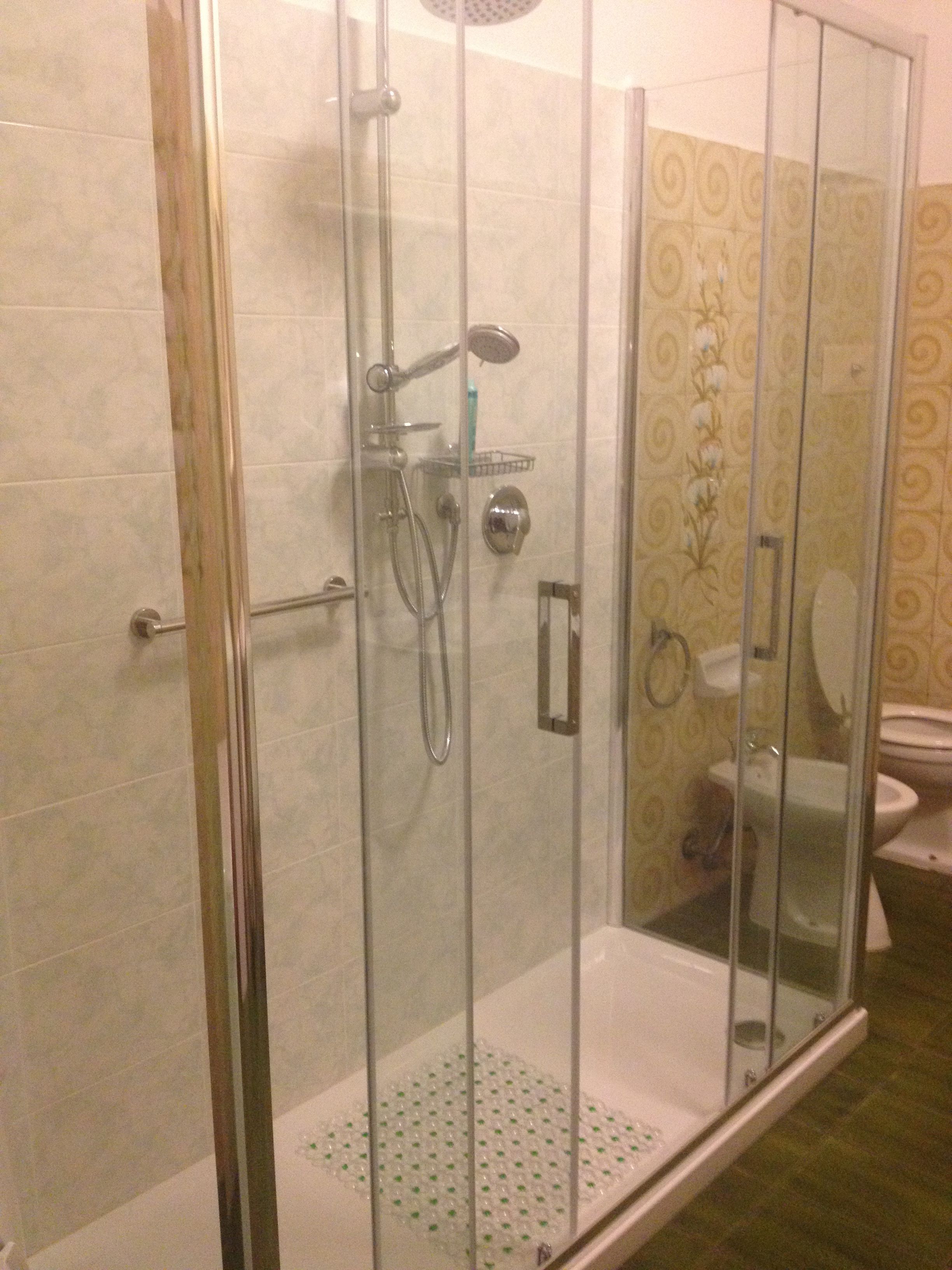 A glass-enclosed shower with a handheld showerhead, a handheld showerhead, and a wall-mounted faucet.