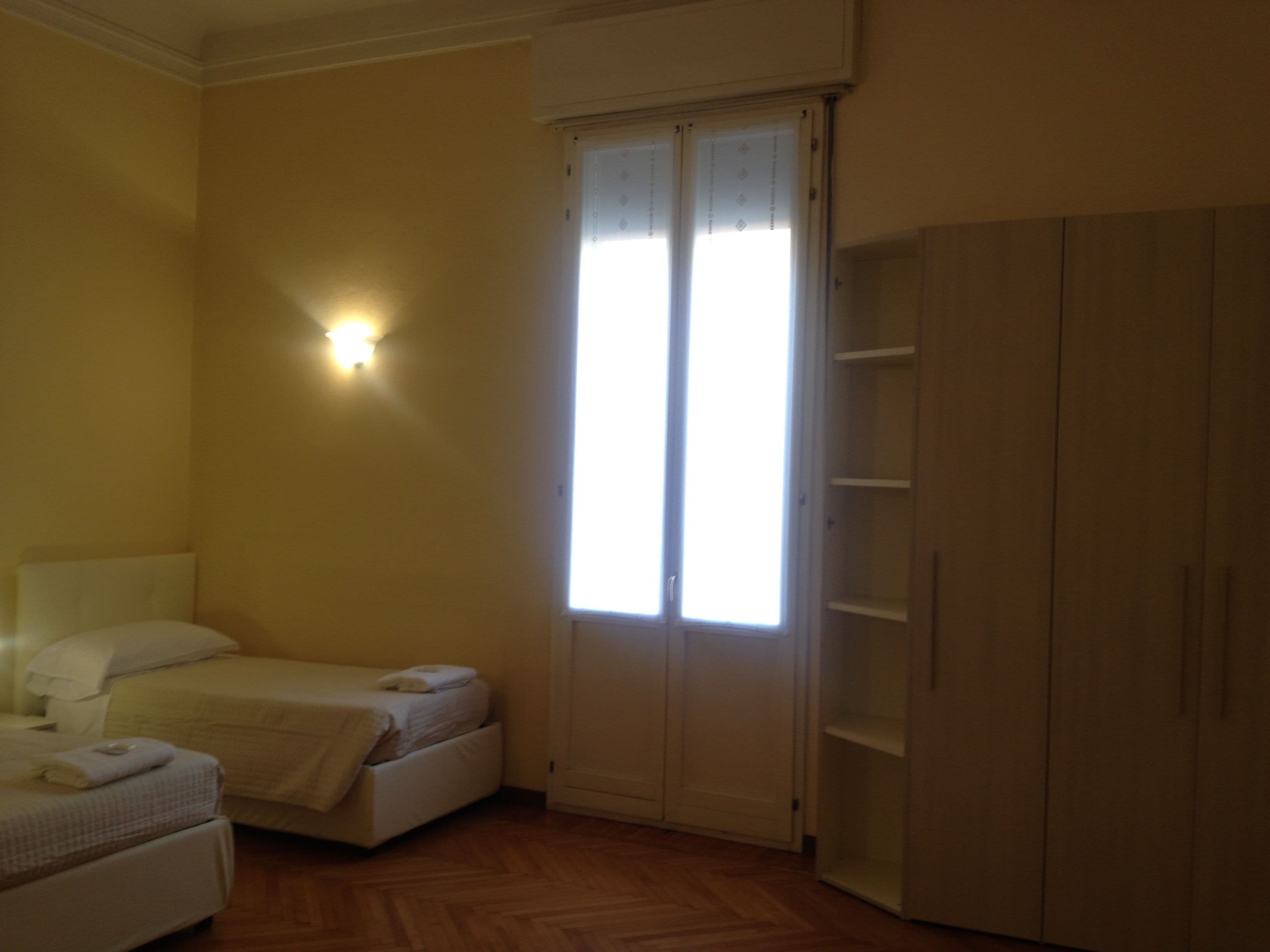 Ein Schlafzimmer mit Bett, Nachttisch, Kleiderschrank und einem Fenster mit Jalousien.