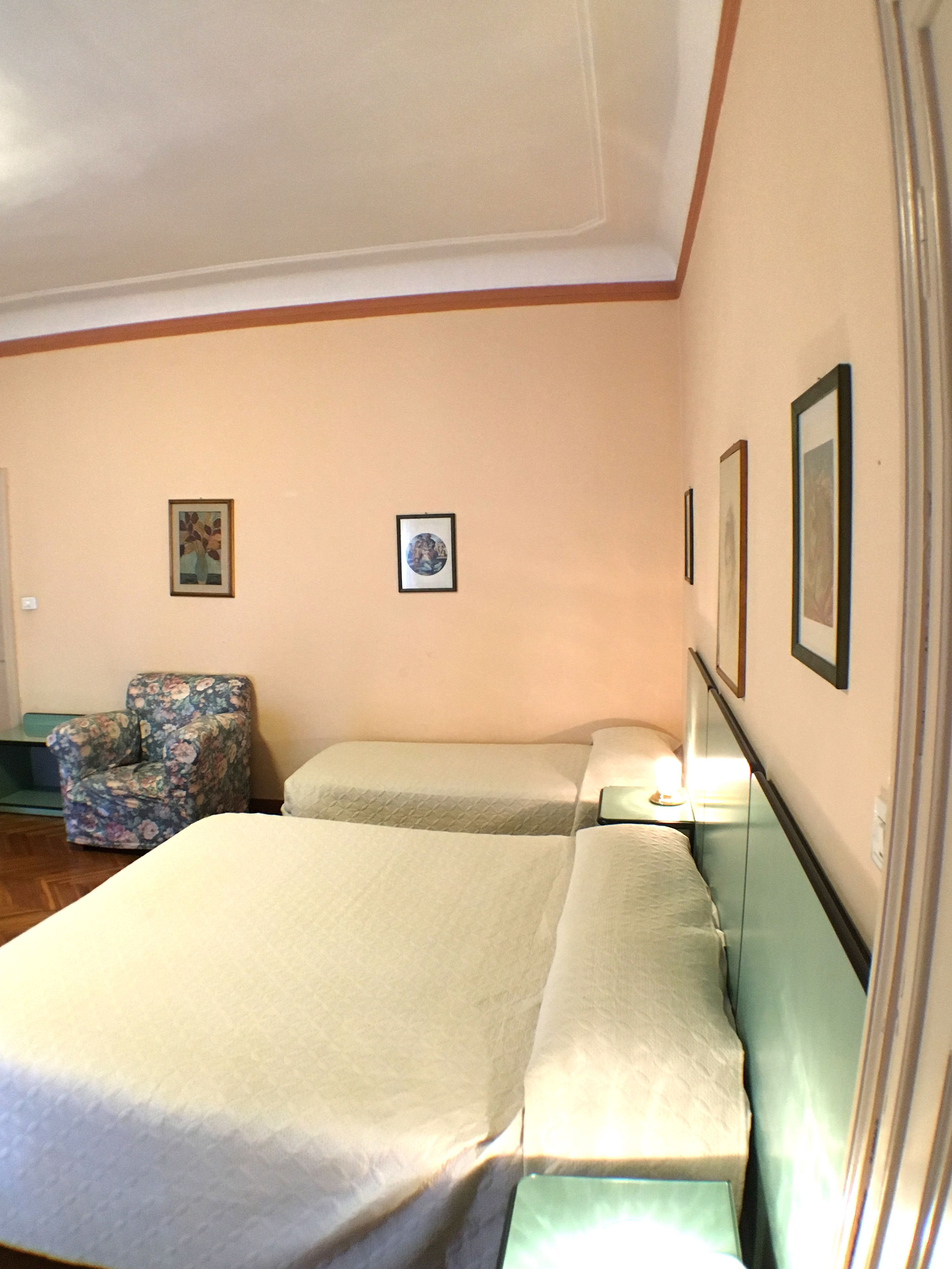 Ein Hotelzimmer mit zwei Betten, einem Sessel und gerahmten Bildern an der Wand.