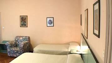 Ein Hotelzimmer mit zwei Betten, einem Sessel und gerahmten Bildern an der Wand.