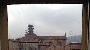 A view from a balcony with terracotta-tiled buildings, a statue, and a construction site in the background. - Albergo Panorama (Bologna)