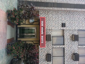 A building with a mosaic tile facade, a sign reading "OUR HOME SUITE," and potted plants with red flowers. - Our Home Suite (Lagos)