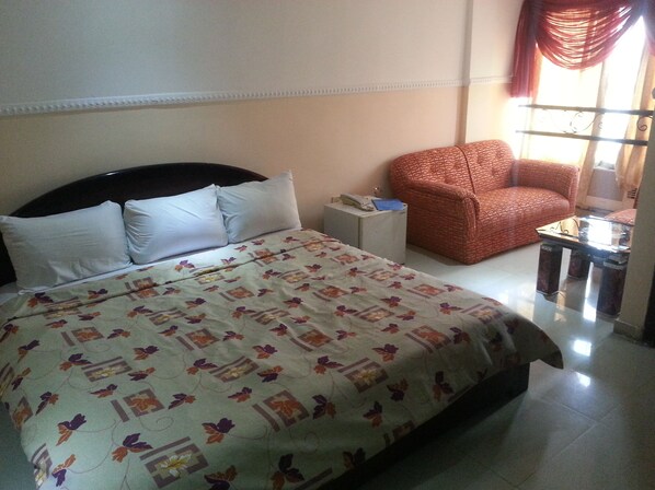A hotel room with a bed, a small side table, a red armchair, and a glass table with a chair.