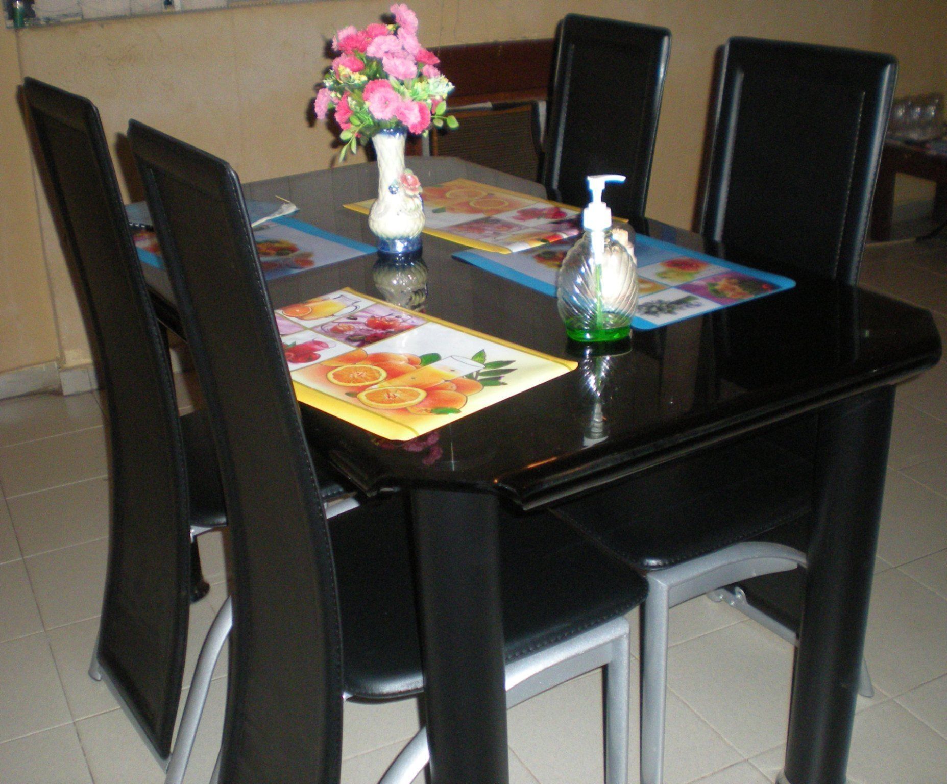 A dining table with a floral centerpiece, a bottle of hand sanitizer, and a placemat with fruit illustrations.