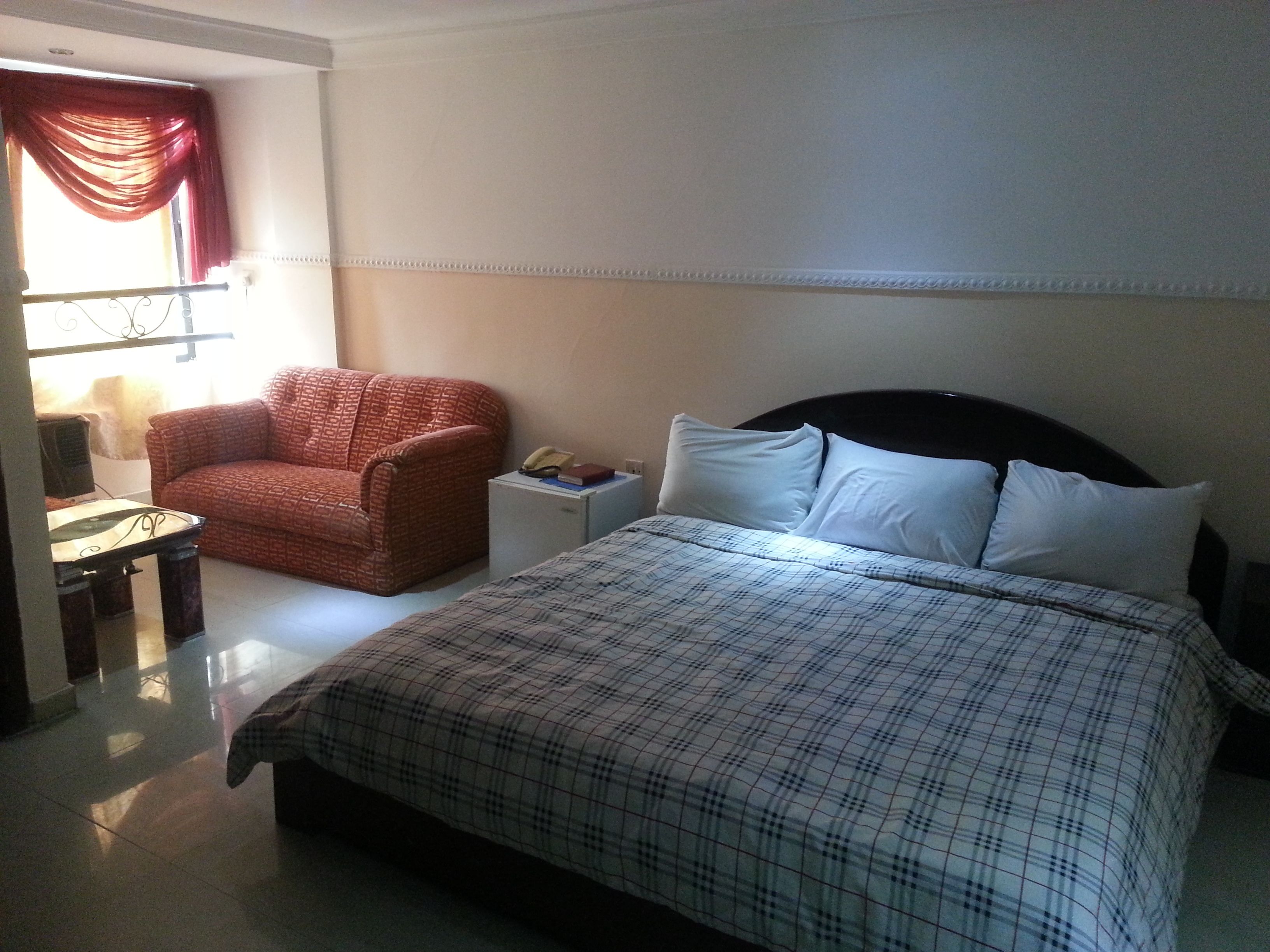 A hotel room with a bed, a chair, a bedside table, and a window with curtains.
