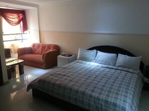 A hotel room with a bed, a chair, a bedside table, and a window with curtains.