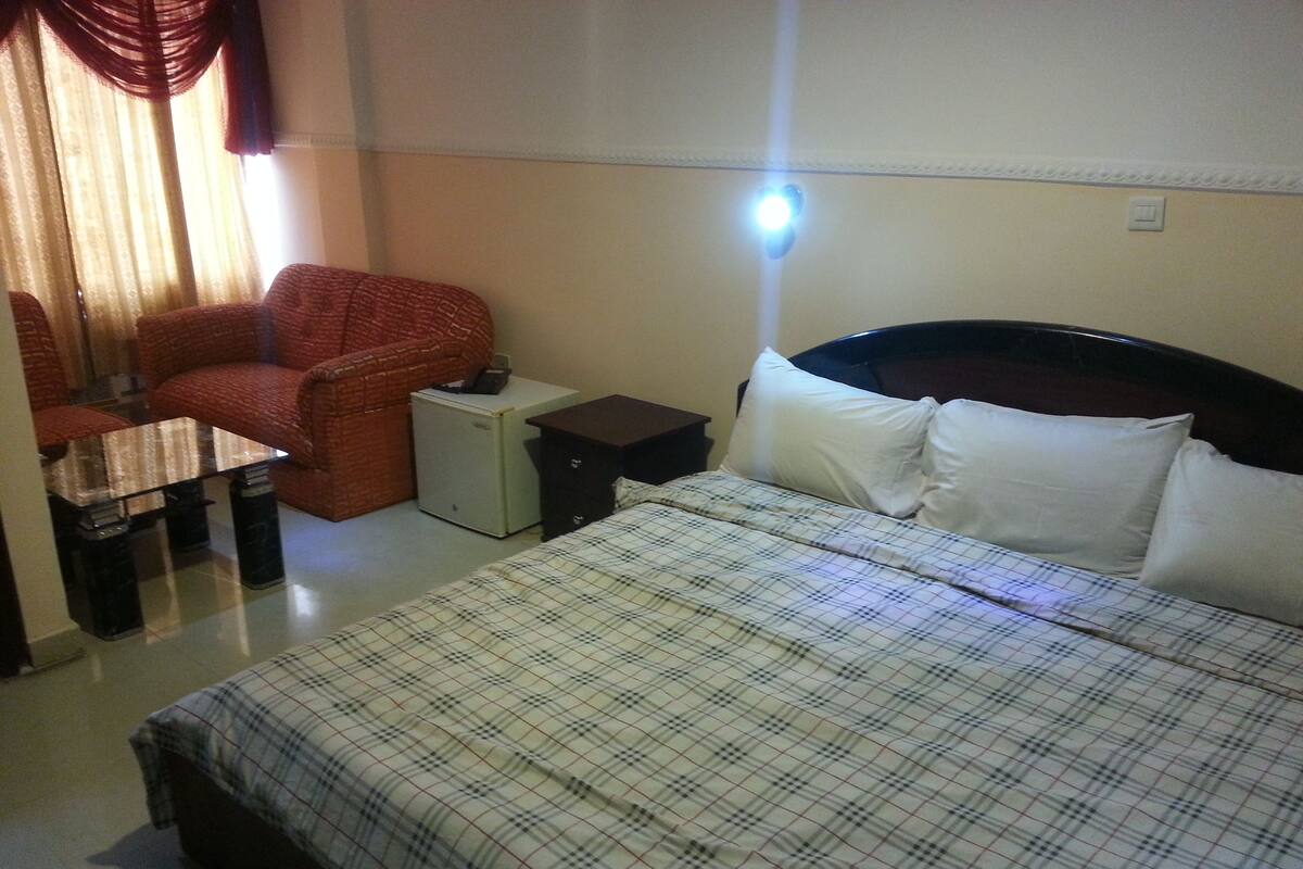A hotel room with a bed, a small desk, a chair, a nightstand, and a lamp.