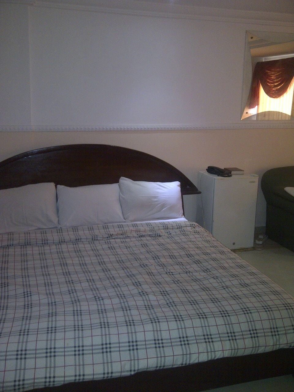 A bed with a plaid bedspread, a wooden headboard, and a white wall.