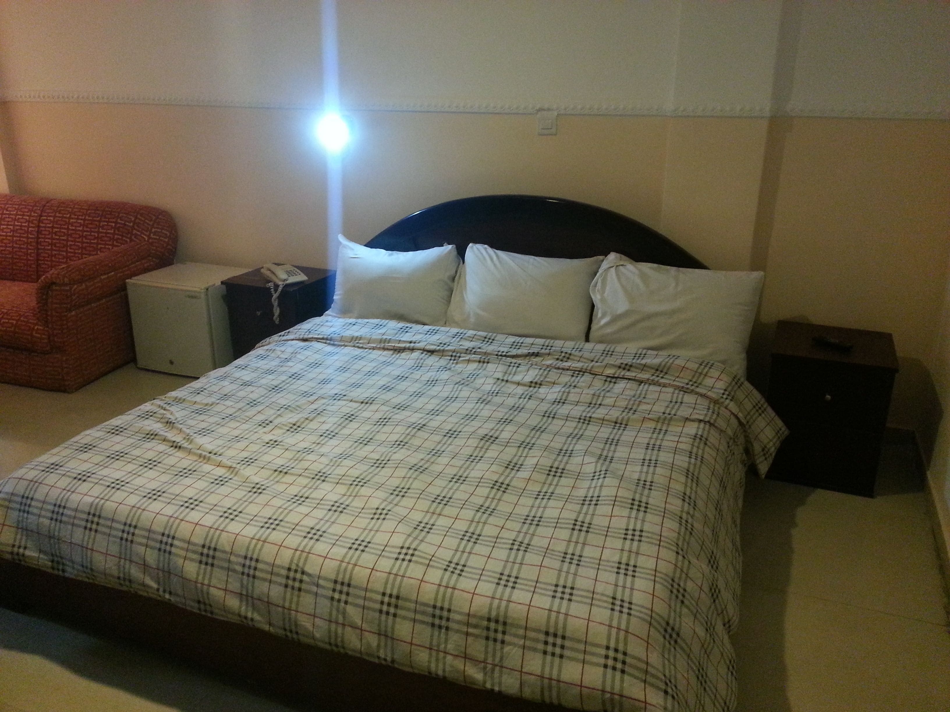 Una habitación de hotel con cama, mesita de noche, silla y mesa auxiliar.
