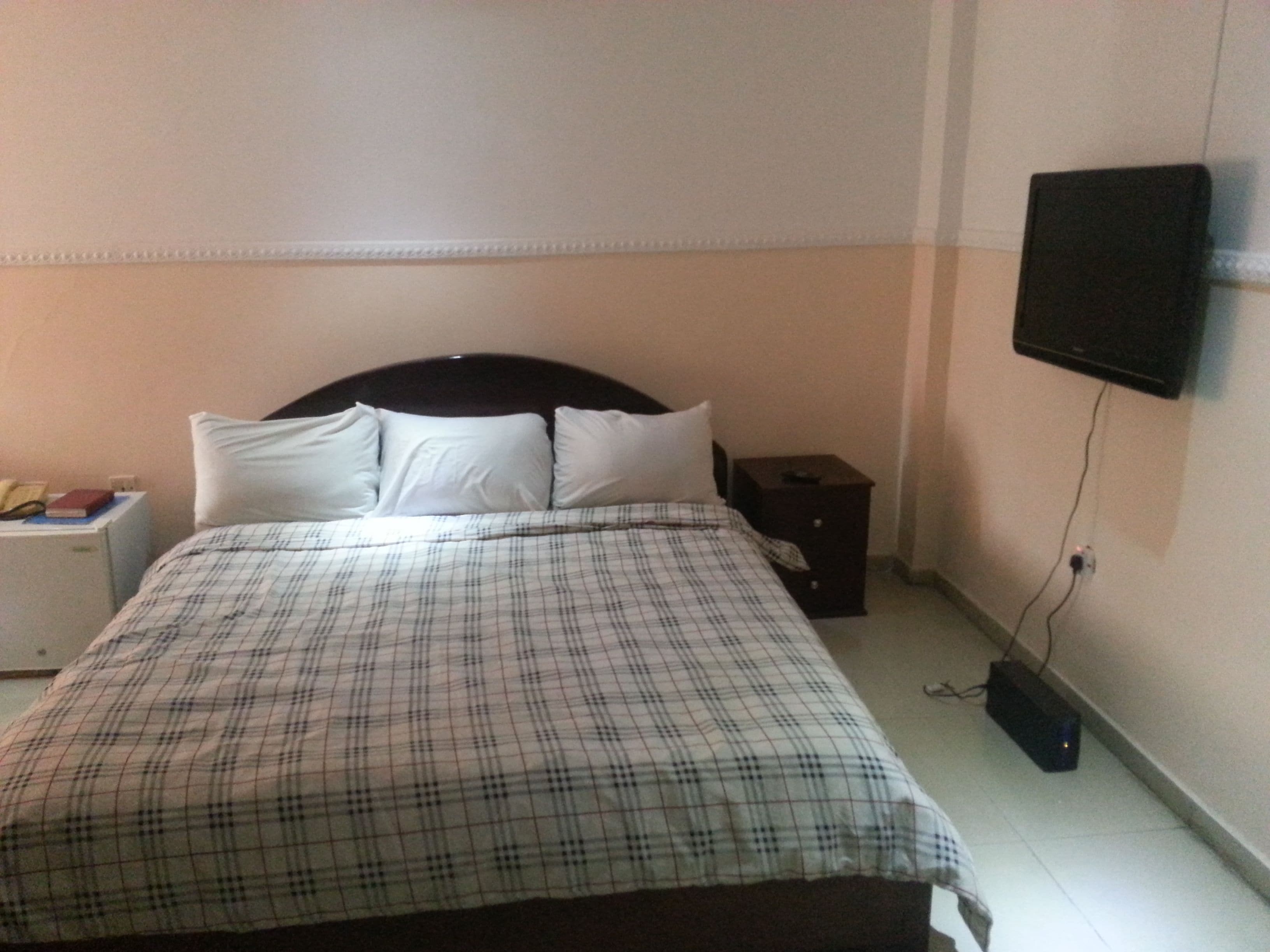 A bedroom with a bed, a nightstand, a TV mounted on the wall, and a power outlet on the floor.