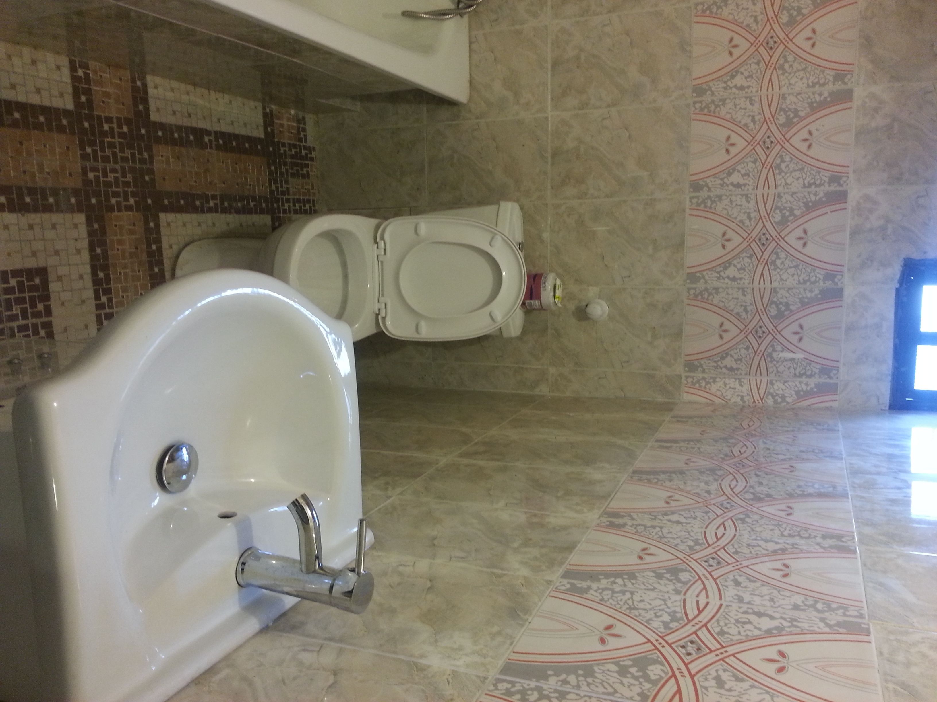 Un baño con inodoro, lavamanos y baldosas de suelo con diseño.
