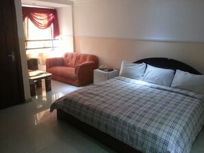 A bedroom with a bed, a chair, a small table, and a nightstand. - Our Home Suite (Lagos)