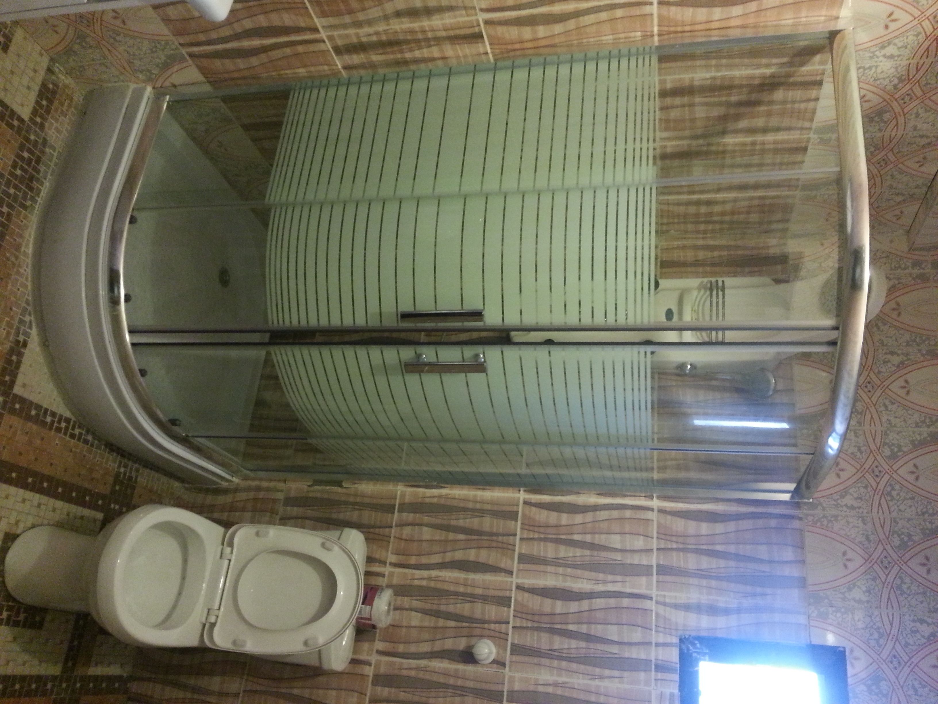 Un baño con inodoro, cabina de ducha de vidrio y baldosas de suelo con diseño.